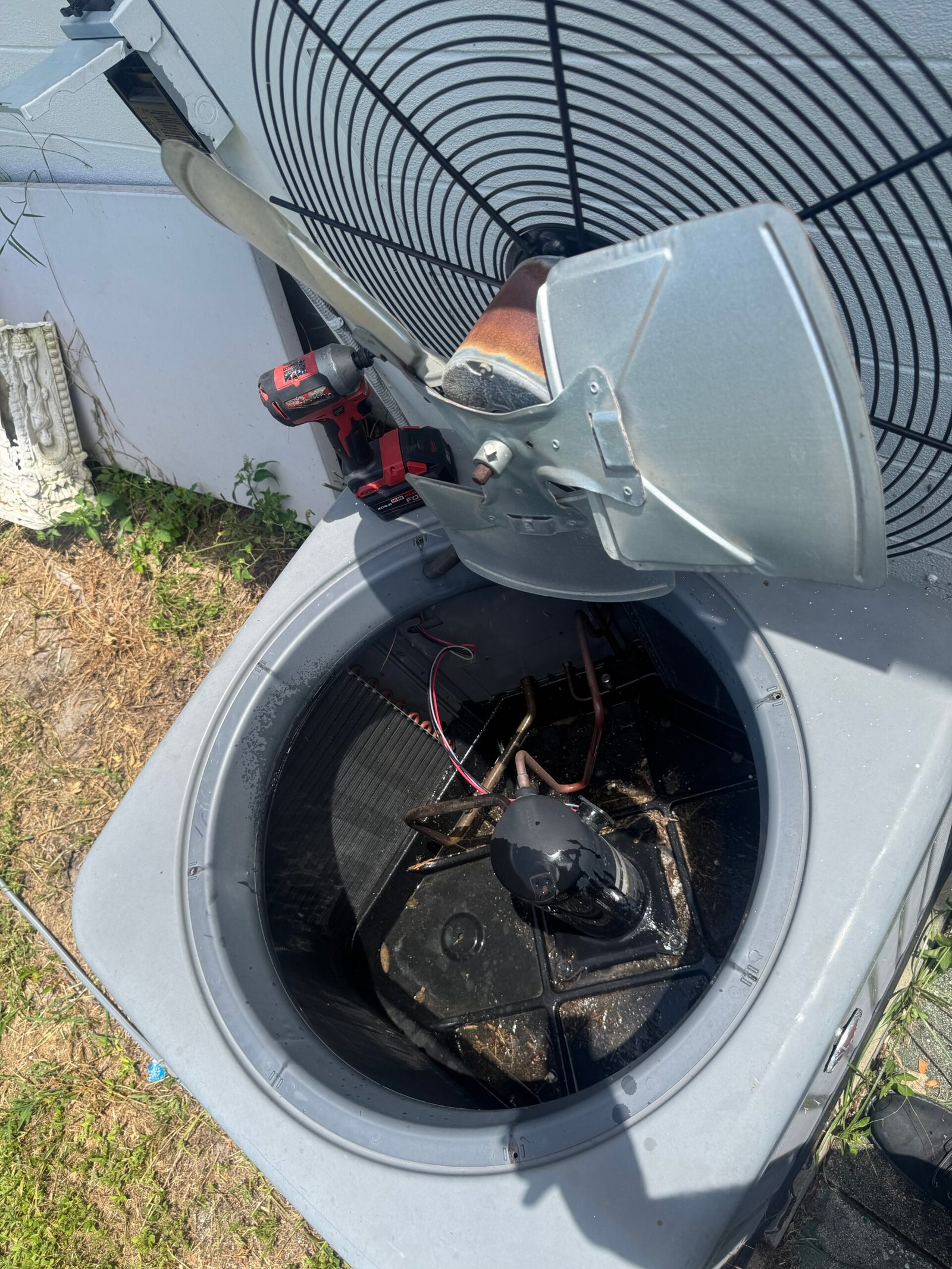 An open outdoor air conditioning condenser unit in Lehigh Acres, Florida, with its top fan assembly lifted to reveal the internal compressor and debris at the bottom, captured during a maintenance service call.