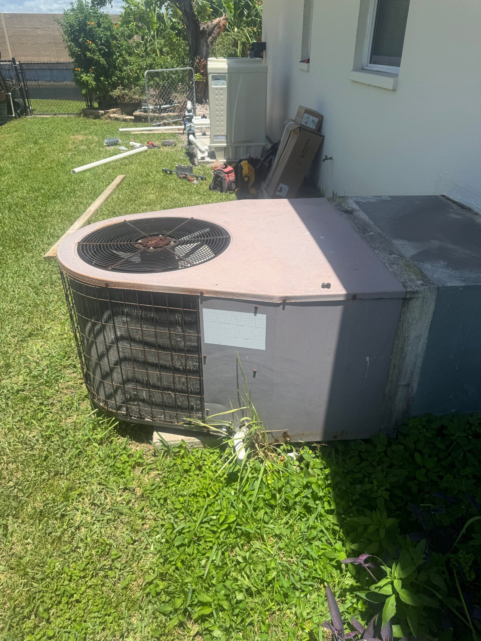 An older, round outdoor AC condenser unit next to a residential building in Cape Coral, Florida, during a tune-up by technician Ryan. Tools are visible in the background.
